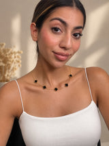 Black clover station necklace worn with a white strappy top, smiling portrait
