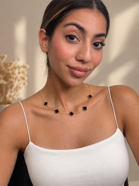 Black clover station necklace worn with a white strappy top, smiling portrait