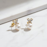A pair of butterfly pearl earrings on a beige surface