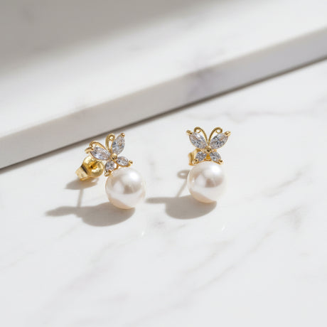 A pair of butterfly pearl earrings on a beige surface