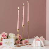 Three lit pink tapers on slim gold rods among roses, tulips and a ribboned box