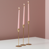 Pencil thin gold rods on flat disc feet carrying three lit soft pink tapers
