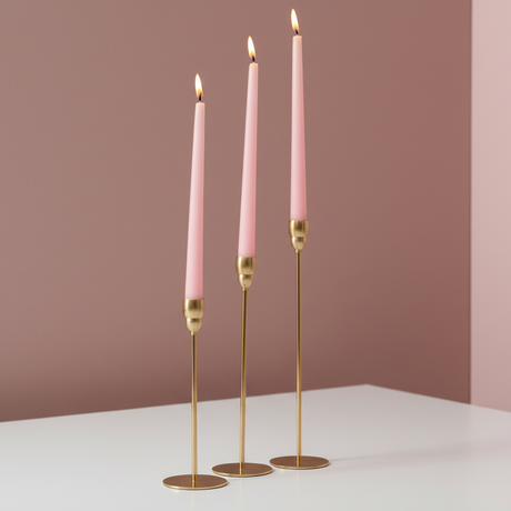 Pencil thin gold rods on flat disc feet carrying three lit soft pink tapers