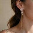 Gold crystal leaf spray earring with long fine chain tassels worn by a woman with a ponytail