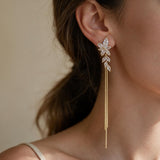 Gold crystal leaf spray earring with long fine chain tassels worn by a woman with a ponytail