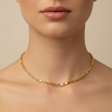 Gold cube necklace worn by a person on a beige background