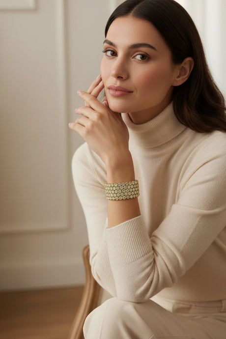 Woman wearing a cream turtleneck sweater and gold bracelet indoors