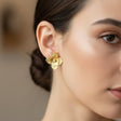 Close-up of a woman wearing gold flower earrings with a blurred background
