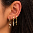 Ear wearing three gold huggies with lightning bolt charms, two crystal and one polished gold