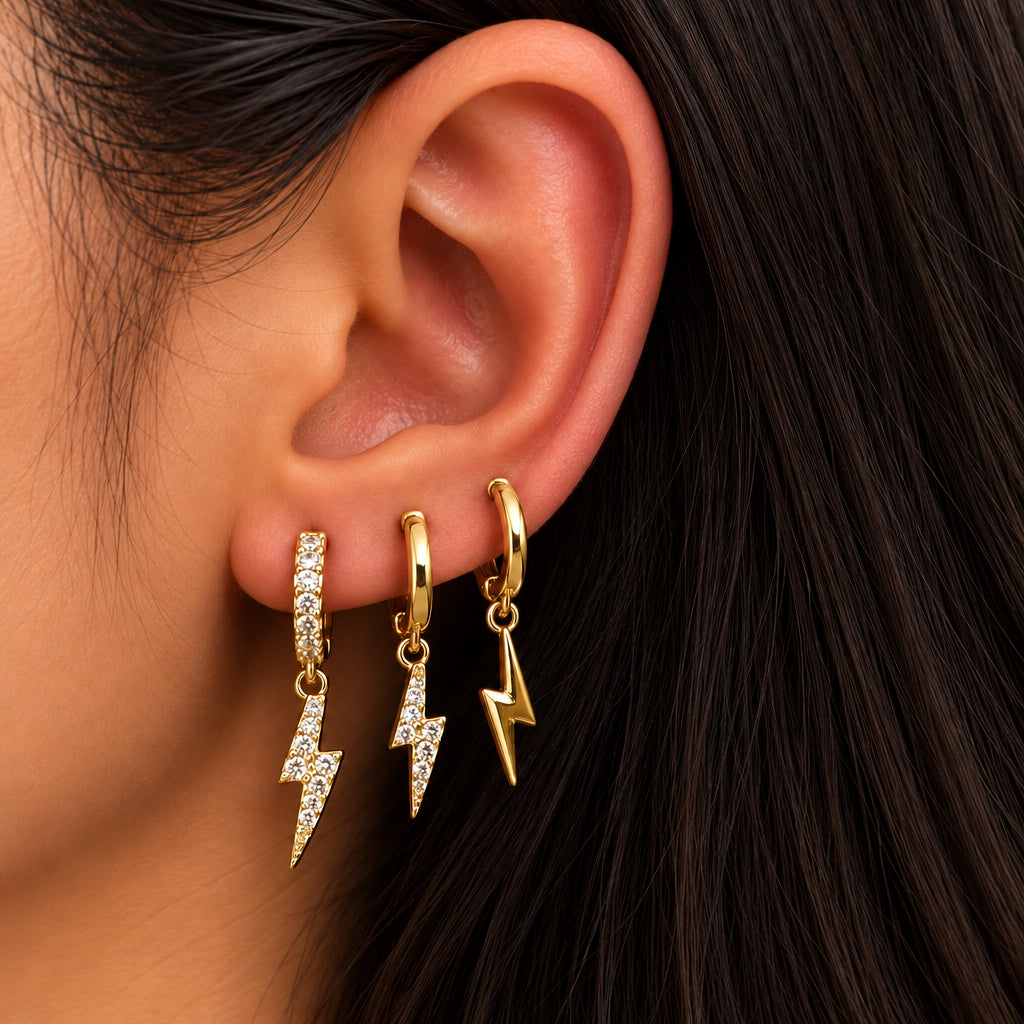Ear wearing three gold huggies with lightning bolt charms, two crystal and one polished gold