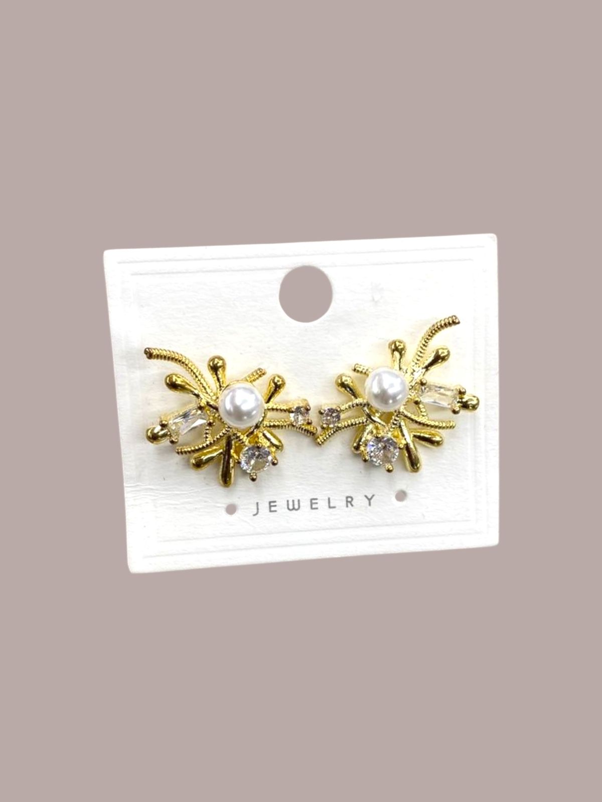 Gold earrings with pearl and crystal accents on a white card against a beige background