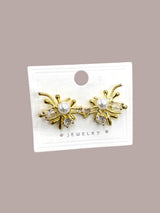Gold earrings with pearl and crystal accents on a white card against a beige background