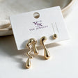 Two gold molten drip studs in different wavy shapes and a small ball stud on a white card