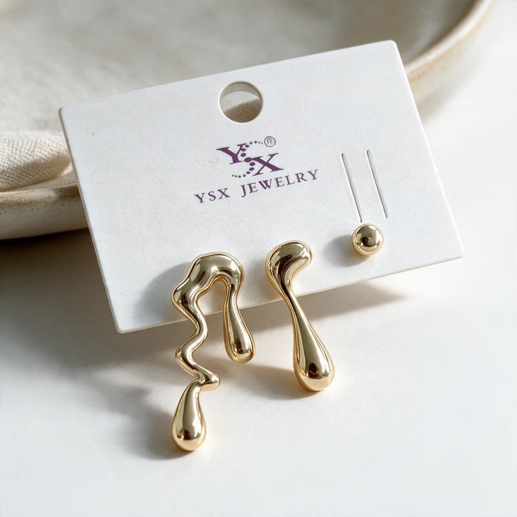 Two gold molten drip studs in different wavy shapes and a small ball stud on a white card