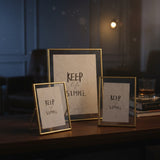 The three gold frames lit against a dark panelled wall beside a cut glass tumbler