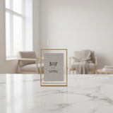 The gold frame small on a marble table in a bright room with two pale armchairs
