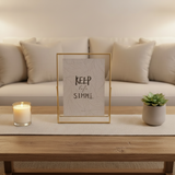 A single gold frame centred on a woven runner between a lit candle and a succulent