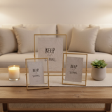 Three slim gold floating frames on an oak table with a candle and a small succulent