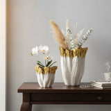 Two sizes of the gold dipped vase on a dark console, one orchid and one with pampas