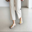 Person wearing white pants, and gold ring handmade sandals in a minimal indoor setting