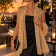 Woman in a black satin dress wearing a sheer gold sequin shawl over her shoulders at a sunset rooftop party