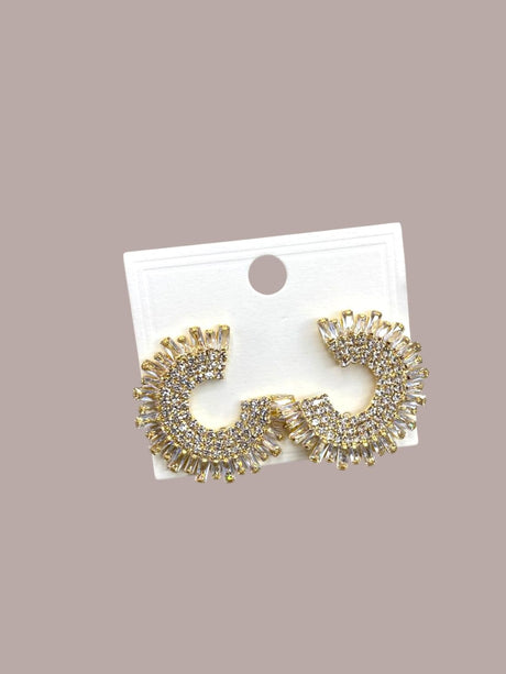 Gold spikey earrings on a white card against a beige background
