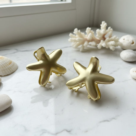 Two matte gold starfish claw clips styled with white coral by a window