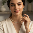 Woman wearing a necklace in a softly lit room with plants in the background