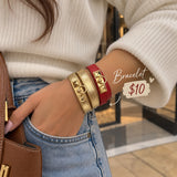 Woman wearing metallic gold and red wrap bracelets with gold pyramid studs, stacked on her wrist with a cream sweater