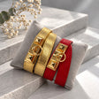 Gold and Red pyramid stud wrap bracelets with gold ring clasps displayed on a grey velvet cushion
