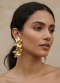 Woman wearing gold floral earrings against a beige background