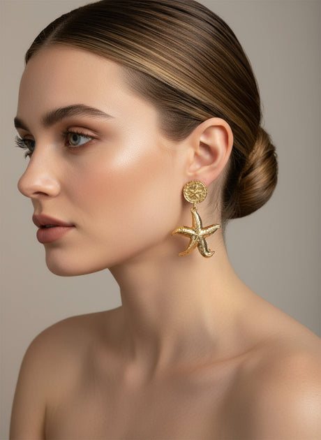 Woman wearing gold starfish earrings against a neutral background