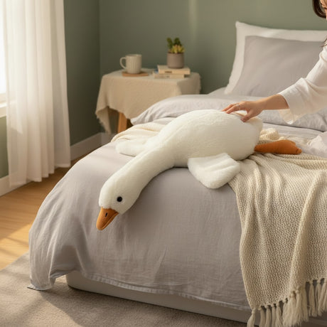White plush goose resting across a bed in a softly lit bedroom