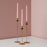 Three gold holders each ringed with a matte black collar, holding soft pink tapers