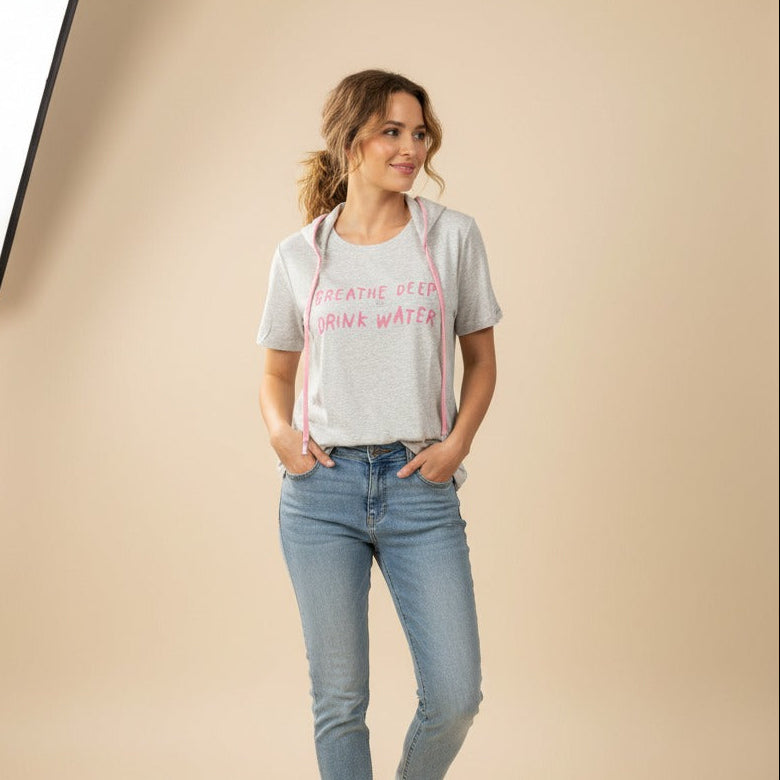 Woman wearing a gray hydration tshirt with pink text and blue jeans on a beige background