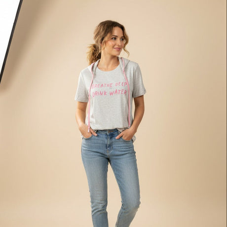 Woman wearing a gray hydration tshirt with pink text and blue jeans on a beige background