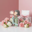 Sage green figure with mint arms and gold spots beside a floral print gift box