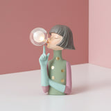 Gold spotted sage dress, pink cuffs and a mint hand pointing up at her lit globe
