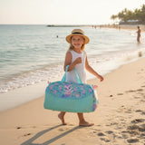 Young girl in a straw hat carrying a turquoise mermaid kitten duffle bag along the shore