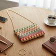 Green chevron tapestry crossbody bag with a gold chain on a table