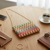 Green chevron tapestry crossbody bag with a gold chain on a table