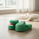 Green plush crocodile slippers with stitched eyes on a wooden floor
