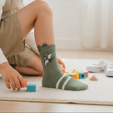 Sage green dinosaur socks with double stripe cuff shown on a wooden floor