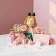 Blonde in a teal green dress, roses resting on her gold pedestal tray among gift boxes