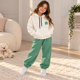 Girl in a white flower hoodie and sage green joggers on a cream rug