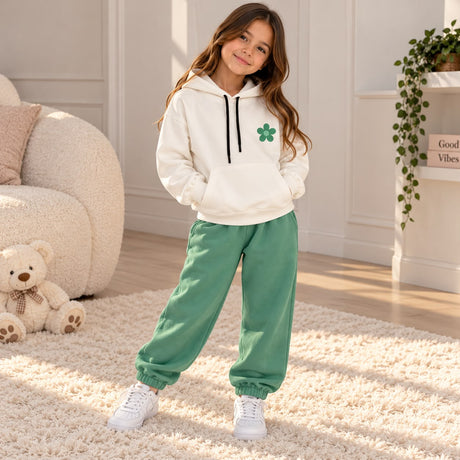 Girl in a white flower hoodie and sage green joggers on a cream rug