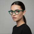 Woman wearing green glasses against a grey background