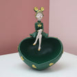 Dark green heart bowl studded with gold hearts, a girl in a green dress seated on the rim