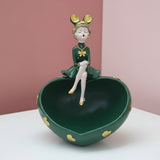 Dark green heart bowl studded with gold hearts, a girl in a green dress seated on the rim