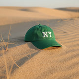 Green embroidered cotton cap on sand dunes with dry grass at sunset